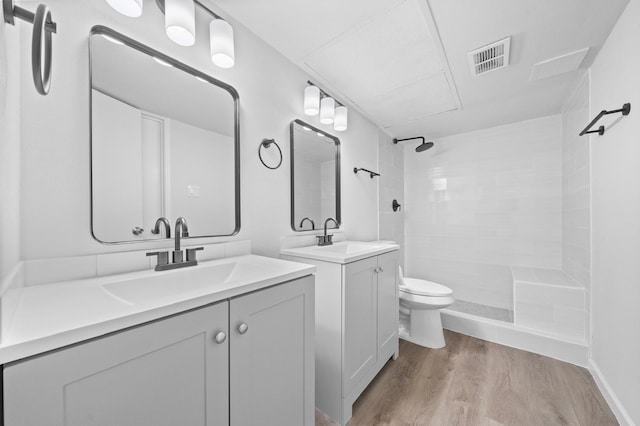 bathroom with tiled shower, vanity, hardwood / wood-style flooring, and toilet