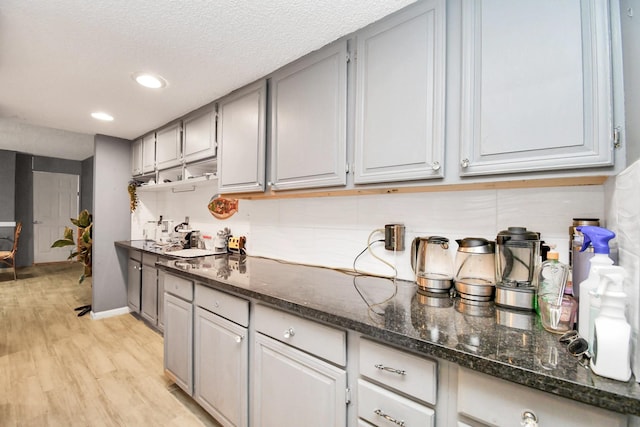 kitchen with a textured ceiling, dark stone counters, light hardwood / wood-style floors, and gray cabinetry