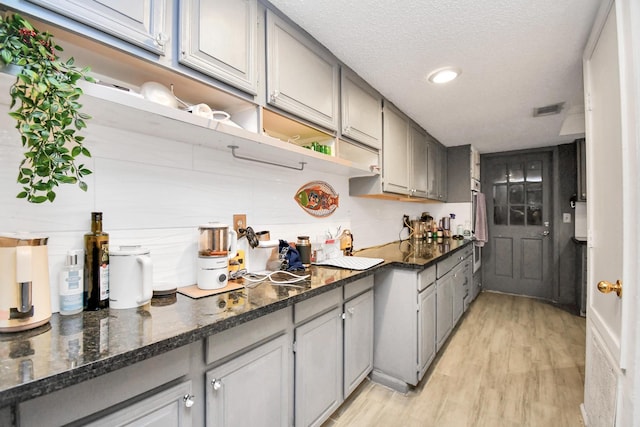 kitchen with gray cabinetry, light hardwood / wood-style floors, a textured ceiling, and dark stone counters