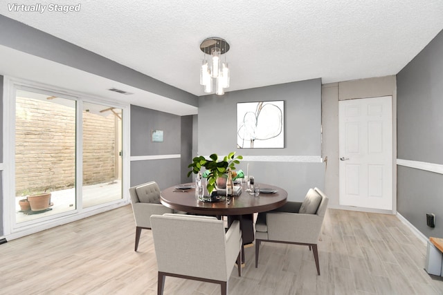 dining area with a notable chandelier, a textured ceiling, and light hardwood / wood-style flooring