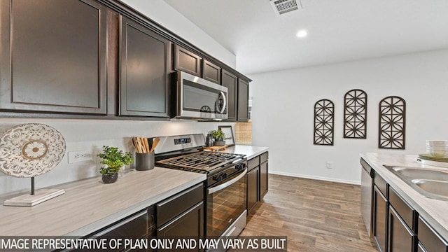 kitchen featuring sink, stainless steel appliances, dark brown cabinets, and light hardwood / wood-style floors