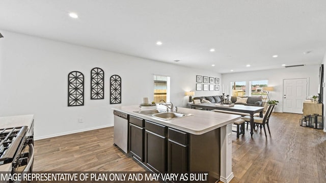 kitchen with appliances with stainless steel finishes, dark brown cabinetry, sink, a center island with sink, and hardwood / wood-style floors