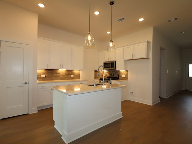 kitchen with a sink, stainless steel appliances, a kitchen island with sink, visible vents, and backsplash