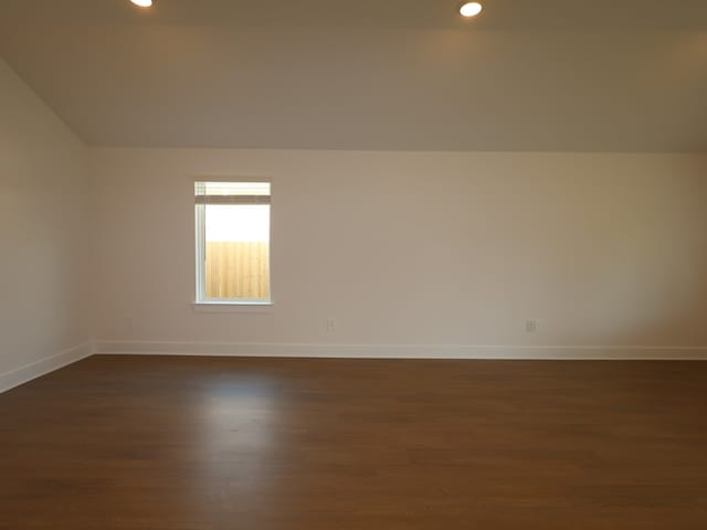 empty room with dark wood finished floors, vaulted ceiling, baseboards, and recessed lighting