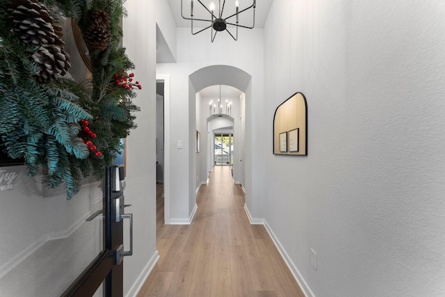 corridor with light wood-type flooring, a high ceiling, and a chandelier