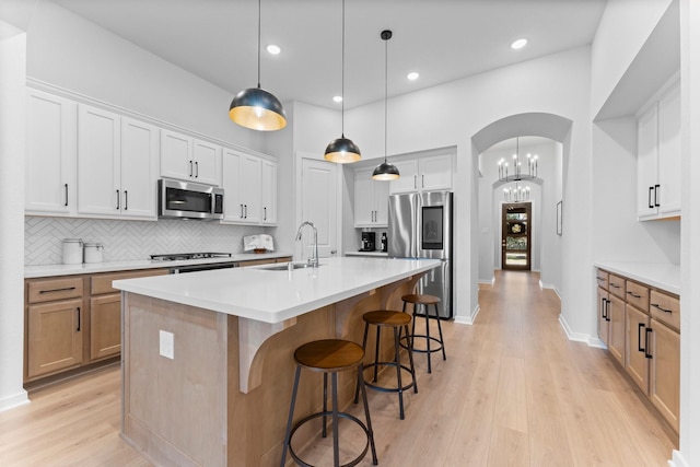 kitchen featuring stainless steel appliances, a kitchen island with sink, decorative light fixtures, white cabinets, and light hardwood / wood-style floors