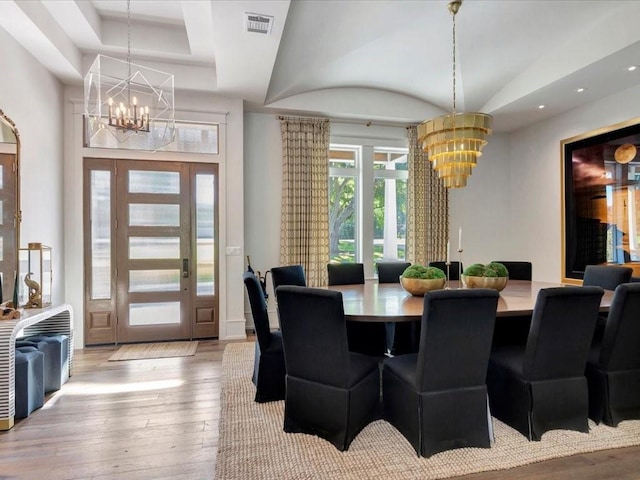 dining space with a chandelier, a tray ceiling, and light hardwood / wood-style flooring