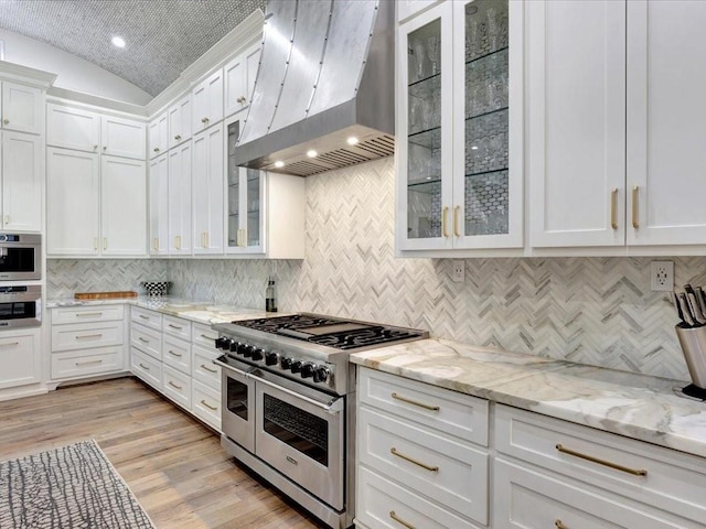 kitchen featuring decorative backsplash, wall chimney range hood, range with two ovens, light hardwood / wood-style floors, and white cabinetry