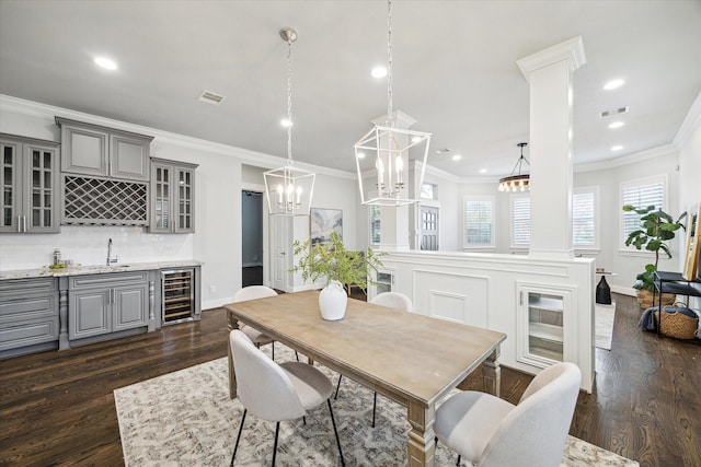 dining room featuring wine cooler, dark hardwood / wood-style flooring, indoor wet bar, decorative columns, and crown molding