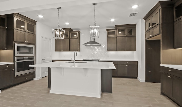 kitchen featuring built in microwave, sink, stainless steel oven, dark brown cabinets, and an island with sink