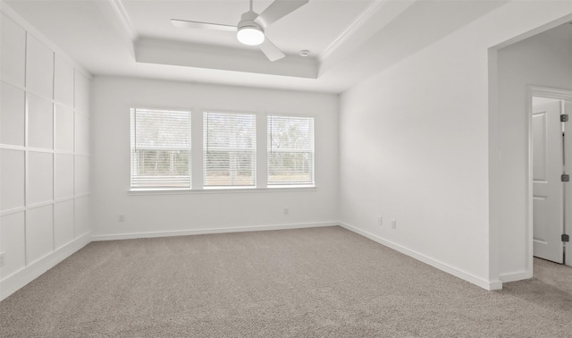 empty room featuring light carpet, a tray ceiling, ornamental molding, and ceiling fan