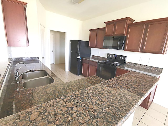 kitchen with sink, kitchen peninsula, dark stone counters, light tile patterned floors, and black appliances