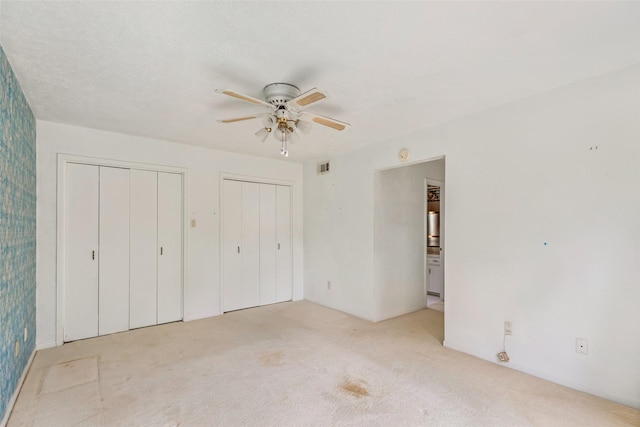 unfurnished bedroom featuring ceiling fan, ensuite bathroom, light carpet, and two closets