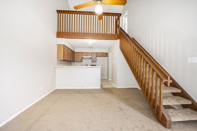 unfurnished living room with ceiling fan, a towering ceiling, and light colored carpet