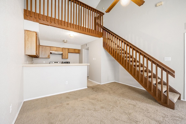 unfurnished living room with ceiling fan, light colored carpet, and a high ceiling