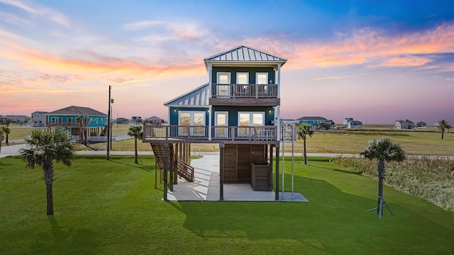 back house at dusk featuring a lawn and a balcony