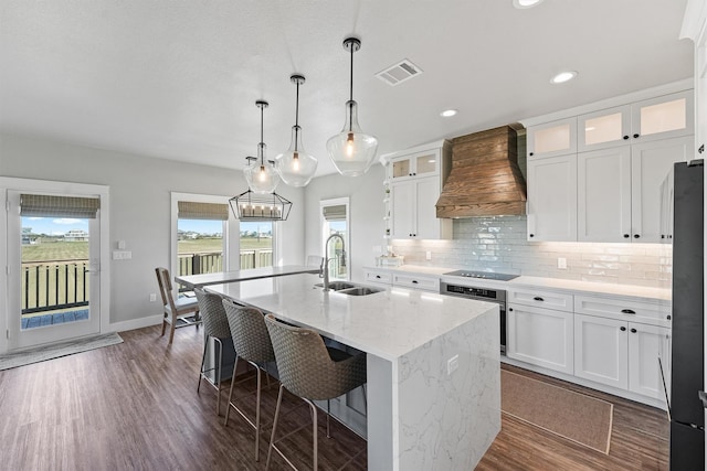 kitchen featuring premium range hood, sink, a center island with sink, white cabinets, and oven