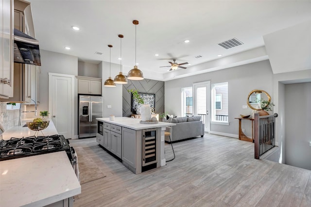 kitchen with gray cabinetry, hanging light fixtures, appliances with stainless steel finishes, a kitchen island, and beverage cooler