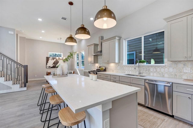 kitchen with sink, wall chimney range hood, gray cabinets, a kitchen island, and appliances with stainless steel finishes