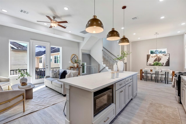 kitchen featuring black microwave, ceiling fan, stainless steel gas range, pendant lighting, and light hardwood / wood-style floors