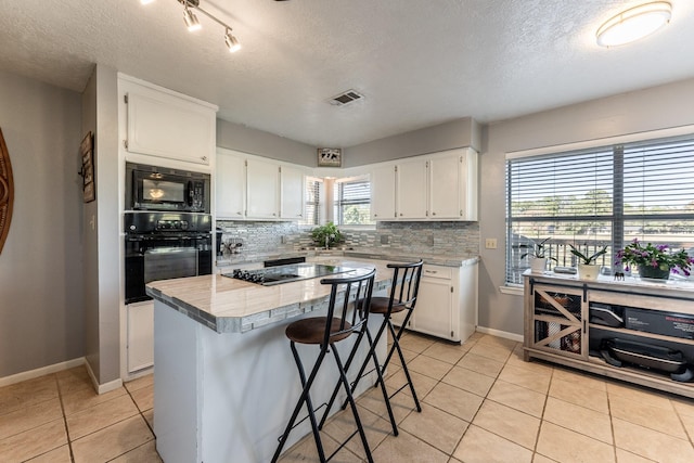 kitchen featuring backsplash, a textured ceiling, black appliances, white cabinets, and a center island