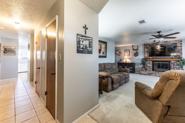 living room with ceiling fan, a fireplace, light tile patterned floors, and a textured ceiling