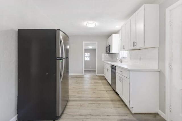 kitchen featuring decorative backsplash, white cabinetry, light wood-type flooring, and appliances with stainless steel finishes