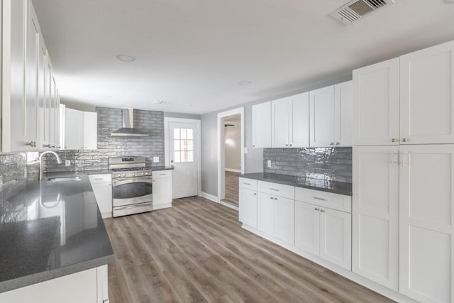 kitchen featuring white cabinets, stainless steel range with gas cooktop, wall chimney range hood, and sink