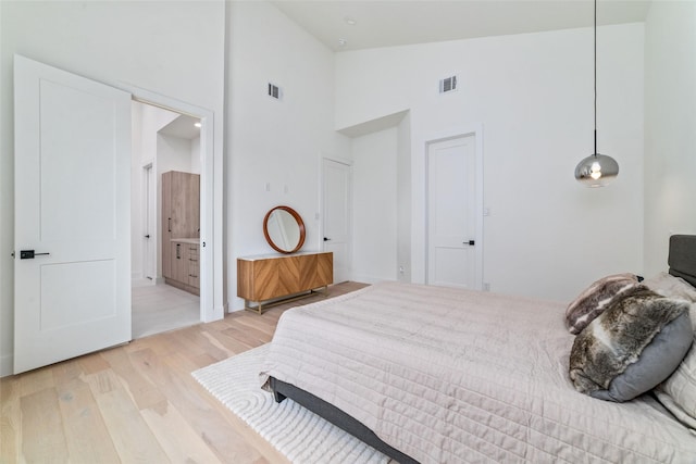 bedroom with ensuite bathroom, high vaulted ceiling, and light wood-type flooring