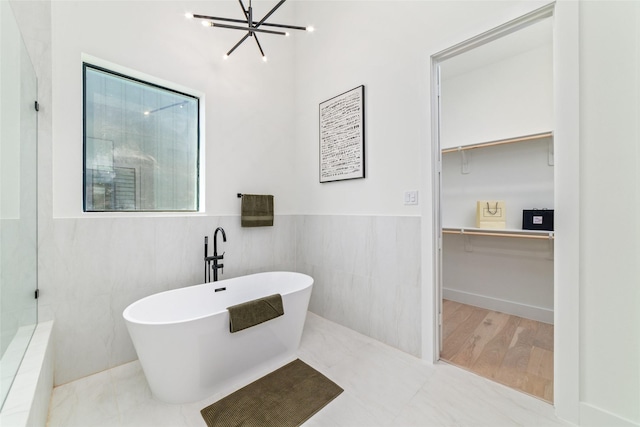 bathroom with wood-type flooring, tile walls, a bathing tub, and a notable chandelier