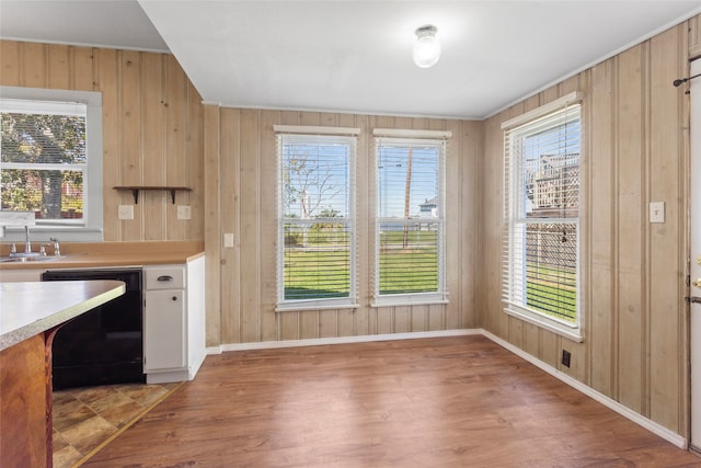 kitchen featuring wood walls, dishwasher, sink, and hardwood / wood-style flooring