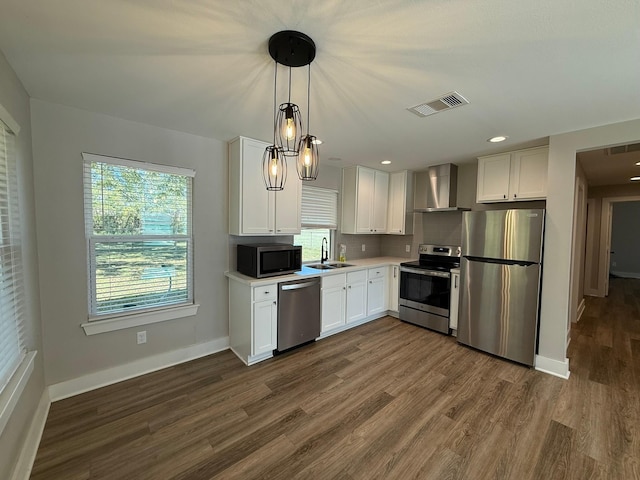 kitchen featuring wall chimney exhaust hood, white cabinetry, hanging light fixtures, and appliances with stainless steel finishes