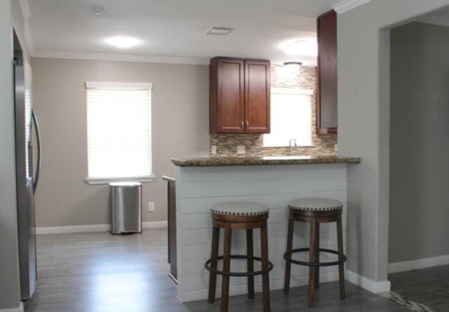 kitchen with tasteful backsplash, dark stone counters, ornamental molding, hardwood / wood-style flooring, and stainless steel refrigerator