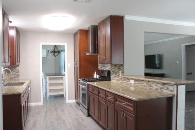 kitchen featuring wall chimney exhaust hood, stainless steel gas range, sink, kitchen peninsula, and backsplash