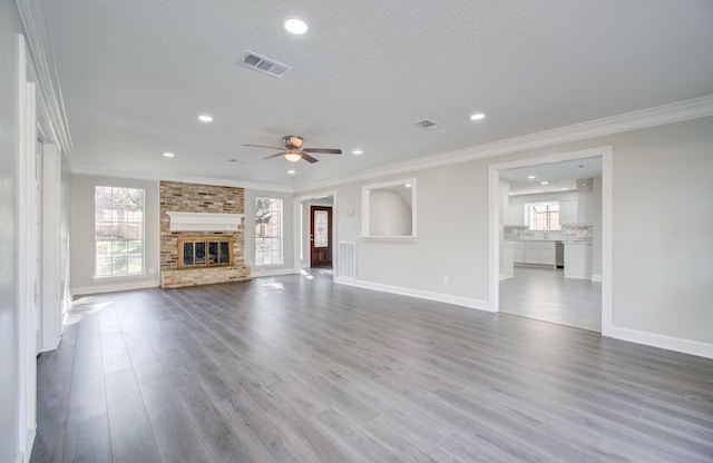 unfurnished living room featuring a textured ceiling, ceiling fan, crown molding, hardwood / wood-style flooring, and a fireplace