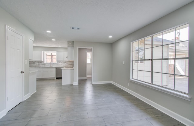 unfurnished living room with sink, a textured ceiling, and light tile patterned flooring