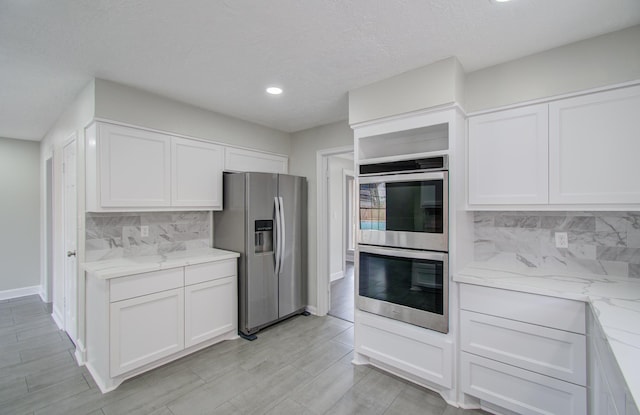 kitchen featuring white cabinets, decorative backsplash, stainless steel appliances, and light stone countertops