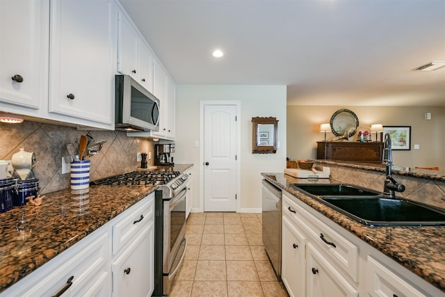 kitchen with appliances with stainless steel finishes, white cabinetry, dark stone counters, and sink