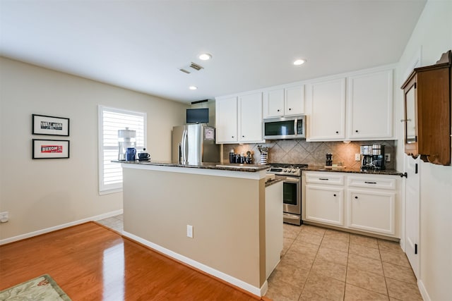 kitchen featuring appliances with stainless steel finishes, a kitchen island, dark stone countertops, light hardwood / wood-style floors, and white cabinetry