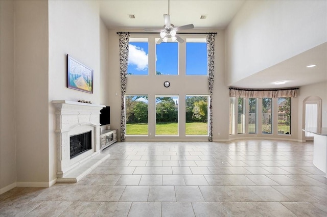 unfurnished living room with ceiling fan, light tile patterned flooring, and a towering ceiling