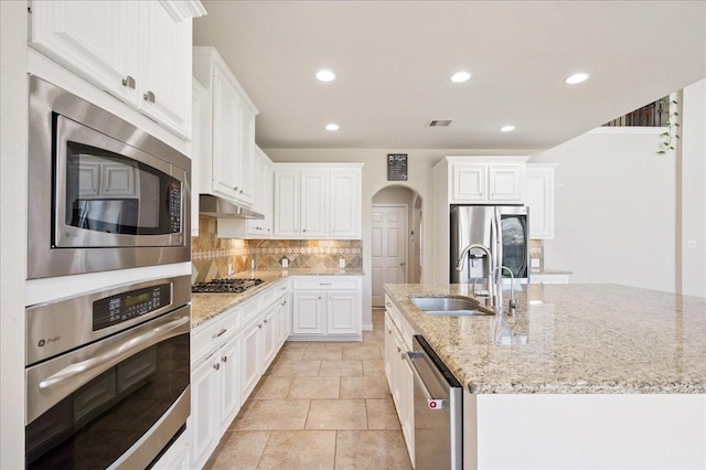 kitchen with light stone countertops, white cabinetry, sink, a kitchen island with sink, and appliances with stainless steel finishes