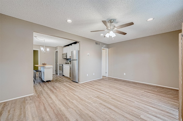 unfurnished living room with ceiling fan with notable chandelier, a textured ceiling, and light wood-type flooring