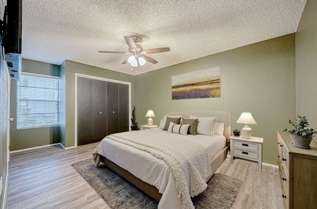 bedroom with ceiling fan, a closet, light hardwood / wood-style floors, and a textured ceiling