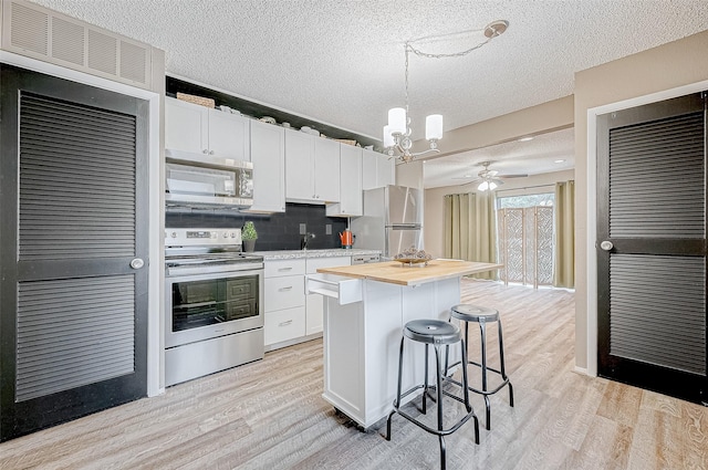 kitchen featuring a center island, hanging light fixtures, white cabinets, ceiling fan with notable chandelier, and appliances with stainless steel finishes