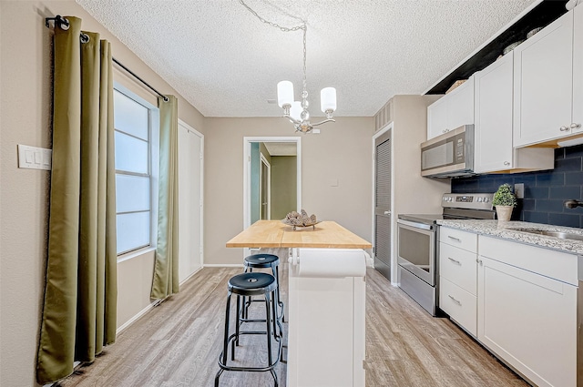 kitchen featuring hanging light fixtures, light wood-type flooring, appliances with stainless steel finishes, a kitchen island, and white cabinetry