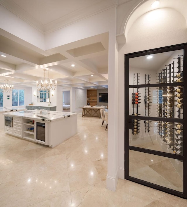 kitchen featuring hanging light fixtures, beverage cooler, coffered ceiling, light stone counters, and ornamental molding