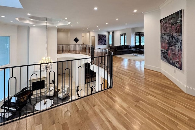 hall featuring a raised ceiling, ornamental molding, light hardwood / wood-style floors, and an inviting chandelier