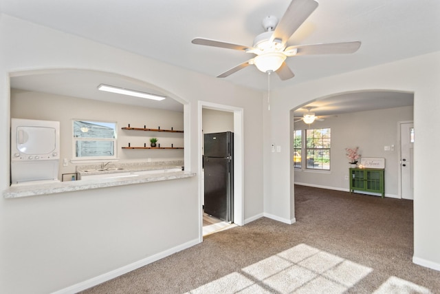 kitchen featuring ceiling fan, black refrigerator, light carpet, and stacked washer and clothes dryer