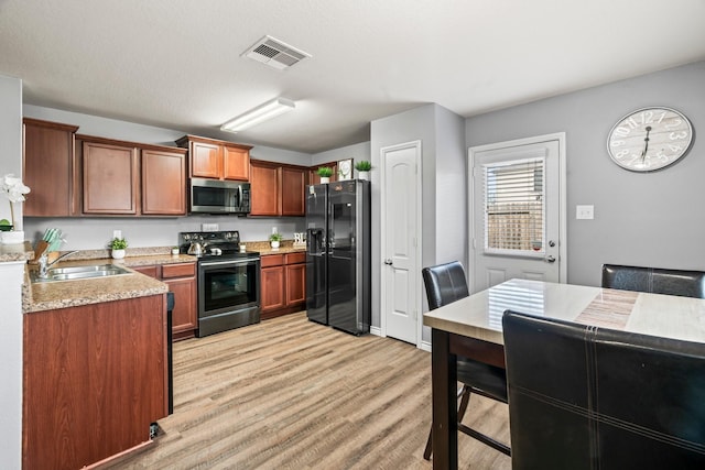 kitchen with black appliances, sink, a textured ceiling, light hardwood / wood-style floors, and light stone counters