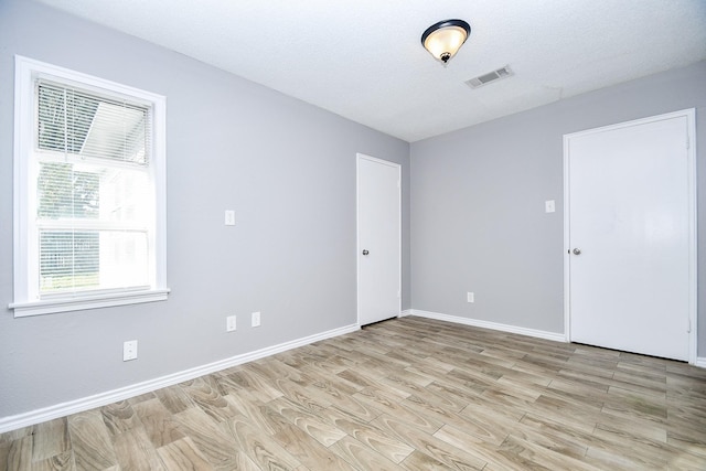 unfurnished room with a textured ceiling and light wood-type flooring